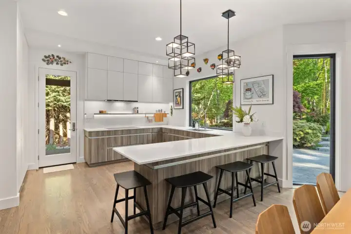 Stunning designer kitchen by Blue Plum- featuring induction cooktop, access to the covered side patio, and the entire wall along the left of this photo is exceptional pantry space! Also notice the extra storage cabinets along the seating area.