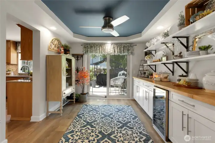 The expanded beverage station adds style and function with butcher block countertops, custom cabinetry, open shelving, a beverage refrigerator, and direct access to the outdoor living space—perfect for entertaining with ease.