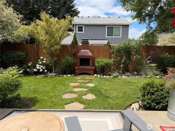 Follow the garden path to a charming outdoor fireplace—an inviting focal point for cozy evenings, quiet mornings, and year-round enjoyment in this beautifully landscaped backyard retreat.