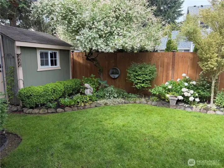 A peaceful garden retreat featuring mature landscaping, seasonal blooms, and a charming storage shed tucked among thoughtfully designed garden beds.