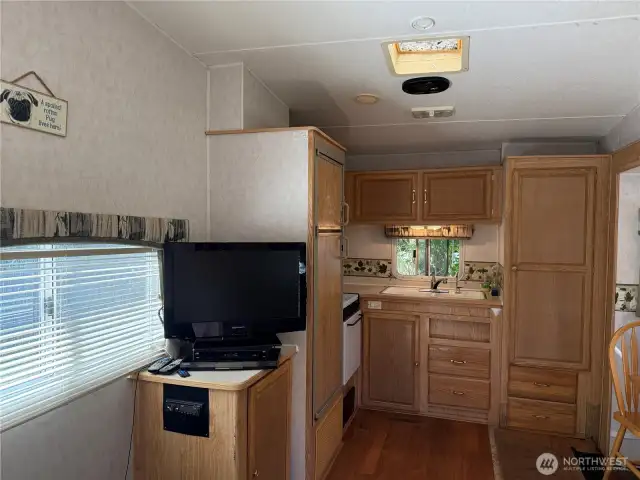 Corner kitchen with large refrigerator, stove, oven and microwave and pantry. Sink looks out to forest.