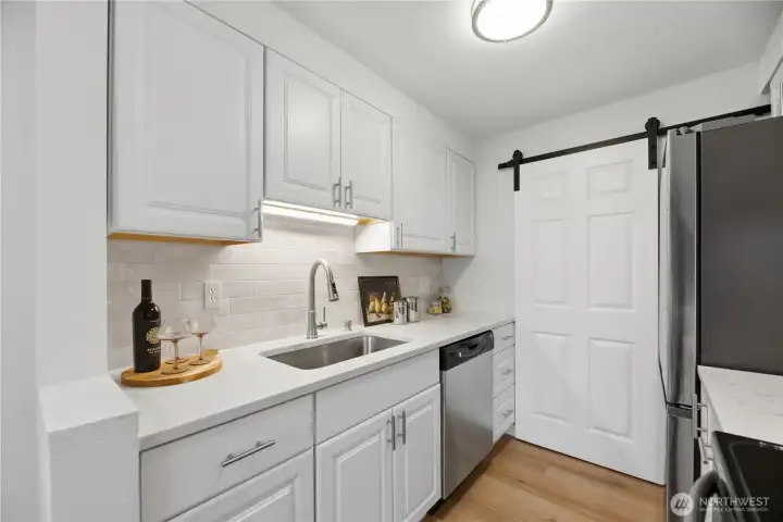 The kitchen features all-new cabinetry, quartz countertops, and a designer backsplash, while the laundry closet is thoughtfully enclosed with a stylish barn door feature.