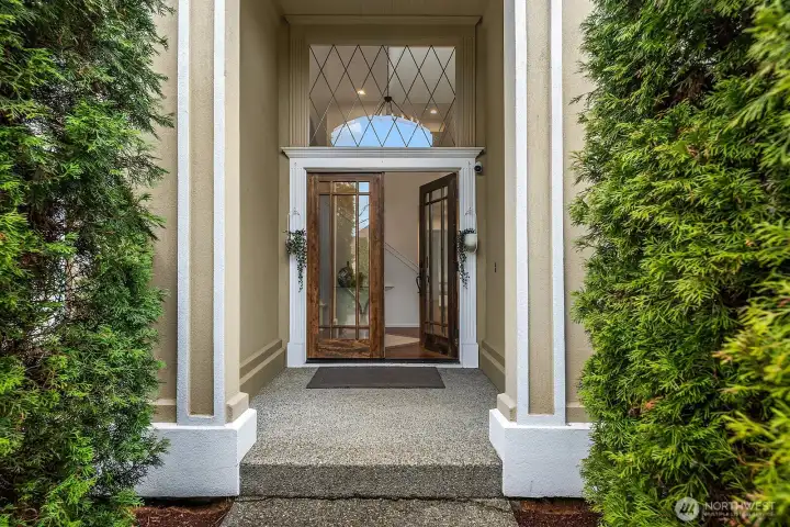 A stunning custom front door welcomes you with soaring covered entry, elegant transom windows, and lush mature landscaping — setting the tone for the refined interiors beyond.