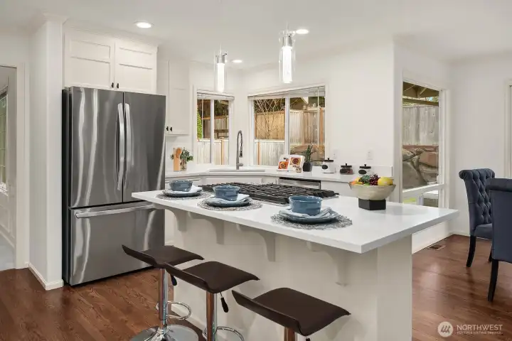 A sleek, well-designed kitchen offers abundant storage, premium stainless steel appliances, and a large island with bar seating, all bathed in natural light from the surrounding windows.
