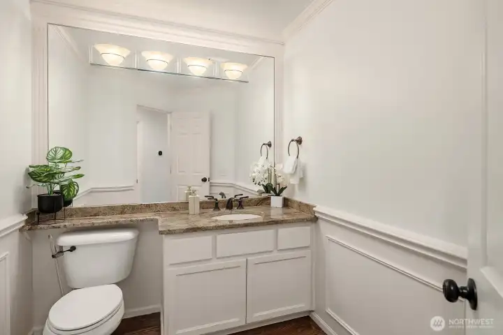 The elegant powder bath features a classic vanity with quartz counters, wainscoting, and refined finishes, a polished and welcoming space for guests on the main level.