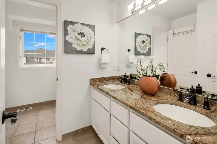 The well-appointed upper level full bath features a dual sink vanity with warm stone countertops and a bright window, offering comfort and convenience for the upper level bedrooms.