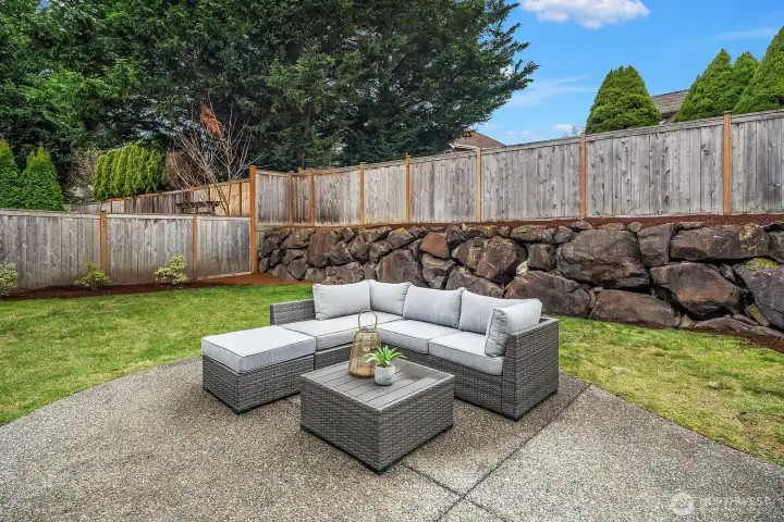 The private backyard offers a wonderful outdoor living space with a cozy patio seating area, lush green lawn, and mature landscaping, perfect for relaxing or entertaining on warm Pacific Northwest days.