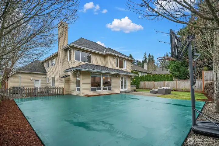 The expansive backyard features a full sports court and is framed by mature trees and privacy fencing, offering exceptional outdoor recreation space rarely found in this coveted Trossachs community.
