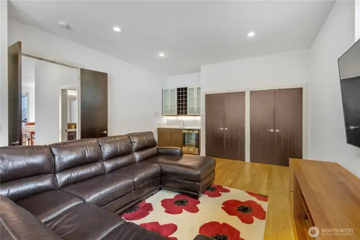 A large media room on the upper floor, behind the living room and kitchen, complete with a wet bar, beverage fridge and wall of deep storage.