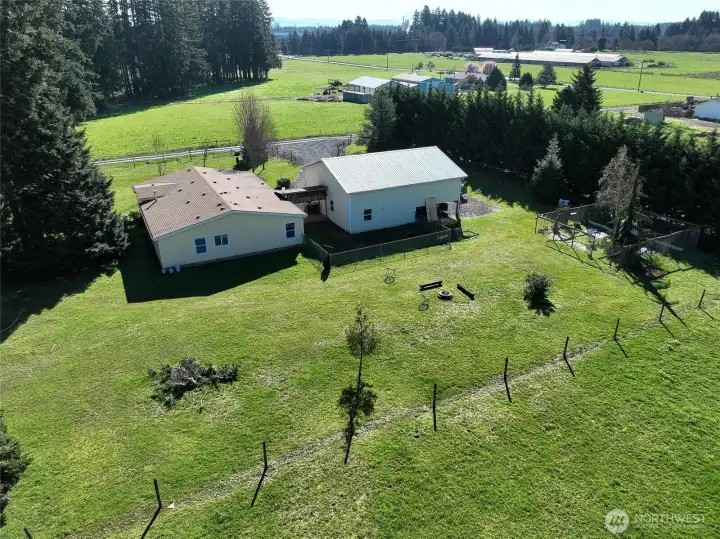 Drone view showcasing the rear of the home, garage, and surrounding acreage.