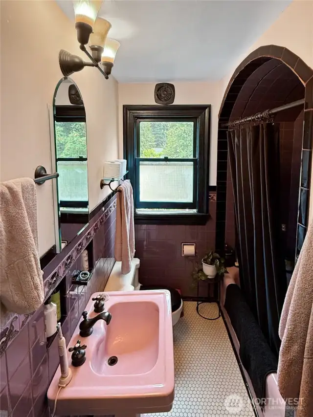 A true blast from the past — in the best way. This bathroom features original 1920s tilework, a statement-making pink sink, and a dramatic arched tub alcove that captures the architectural whimsy of the era. With charming hex tile underfoot and updated lighting above, it’s full of personality and potential. Embrace the retro flair, or make it your own — either way, the bones are timeless.