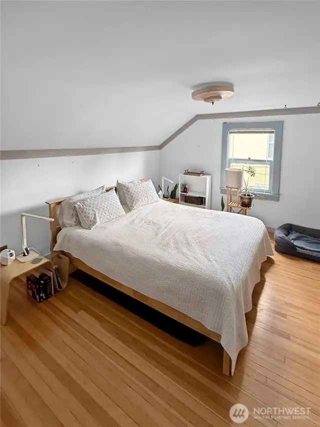 Tucked beneath the eaves, this upstairs primary bedroom was made for slow, cozy mornings and restful nights. The sloped ceiling adds architectural charm, while original hardwood floors and soft natural light bring warmth and calm. Whether you lean into the vintage character or update with your own flair, this peaceful retreat is ready to rise and shine.