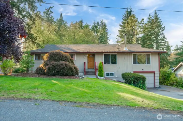 Classic daylight basement rambler surrounded by mature trees and lush greenery, offering a peaceful, established neighborhood setting. The main-level entry provides easy access with welcoming curb appeal and a timeless exterior.