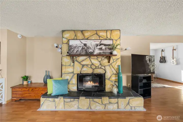 A striking stone fireplace anchors the room and adds warmth and character, serving as the perfect focal point for family gatherings. The generous hearth doubles as additional seating or display space, blending charm with function.