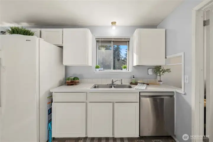 Window over the double-bowl sink brings in natural light; tile counters and upper/lower cabinets keep essentials organized.