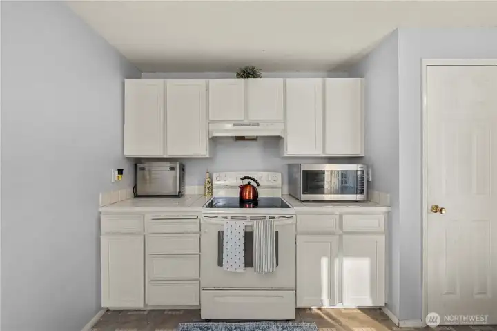 Cooking zone features an electric range with vent hood, a bank of drawers for utensils, and a nearby closet pantry for extra storage.