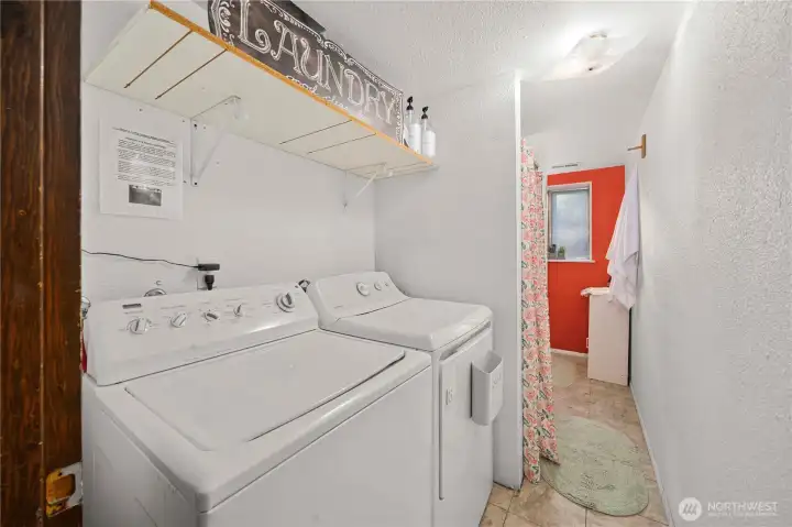 Convenient lower-level bath and laundry combo offers practical functionality, featuring full-size washer and dryer, open shelving for storage, and easy access from the adjacent living areas.