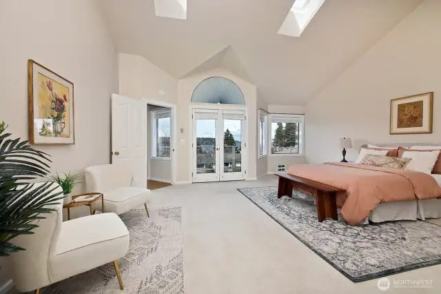 Vaulted ceilings, sky lights, windows, your own private waterside balcony in this primary suite. Double glass doors ahead open to a balcony. Your back is to the full bath and your walk-in closet.