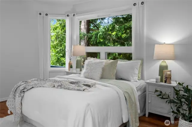 Light-filled main floor primary bedroom with serene forest views creates a restful, calming atmosphere.