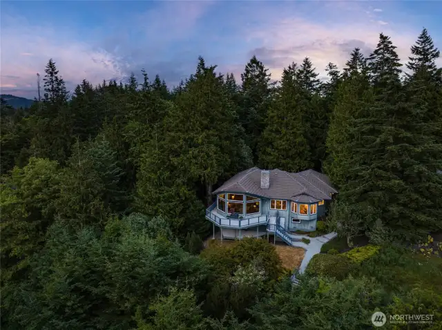 With sweeping views of Puget Sound, tucked into the trees and aglow at dusk, this architecturally striking home offers a warm welcome and rare privacy—where forest serenity meets elevated living.