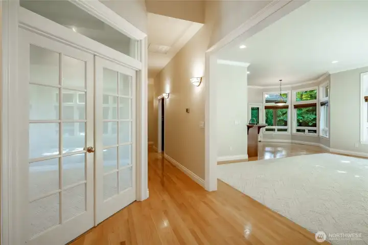 View down the hall toward the Primary Bedroom. Office on the left, living room to the right. Kitchen and dining area in the background. Bedroom 1 & 2 behind the photographer.