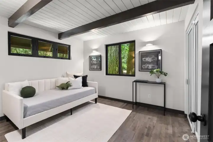 Unwind in a space where modern design meets the calm of the woods. This light-filled second bedroom on the main level offers a unique, tranquil escape. The dark wood beams and clean wood ceilings frame private, lush forest views through dual picture windows. It’s the perfect backdrop for a restorative retreat—a space that’s both cozy and architecturally striking.