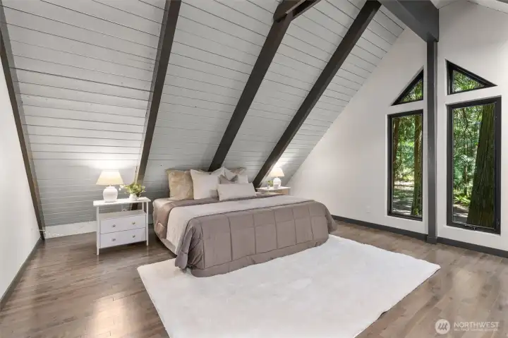 Welcome to a primary suite that feels like a boutique luxury hotel. Architecturally spectacular, this grand sanctuary boasts soaring, sharply angled cathedral ceilings lined with clean white planking and anchored by bold dark beams. Geometric accent windows frame peaceful views of the surrounding treetops, filling the room with soft, natural light.  ?The luxury continues with a massive his-and-hers walk-in closet fully equipped with custom built-in shelving to keep your wardrobe flawlessly organized.