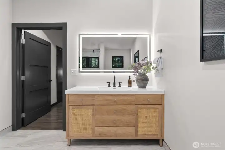Just steps away, the gorgeous ensuite bathroom serves as your private spa—featuring a beautiful light wood vanity with caned-front accents, modern matte-black hardware, an LED-backlit mirror, and a pristine subway-tiled tub and shower. It’s a masterfully designed space dedicated entirely to rest and rejuvenation.