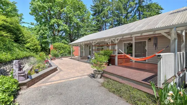 Relax on the sheltered backyard porch, perfect for lounging or hanging a hammock. A short staircase descends to a paved walkway, surrounded by thriving greenery - this space offers a calm and refreshing atmosphere.