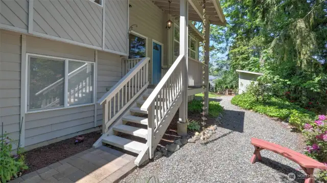 As you approach the entrance, a set of stairs welcomes you, surrounded by beautifully placed gravel, vibrant flowers, and lush greenery.