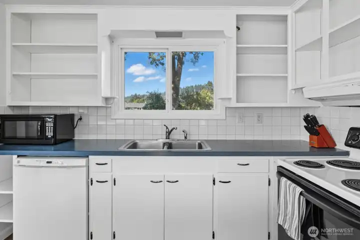 Kitchen with open shelving, ceramic tile backsplash and views to the back yard.