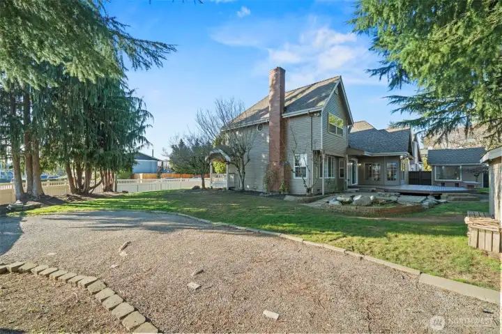 Rear exterior of the home featuring a large deck, patio seating area, and generous yard framed by mature landscaping.