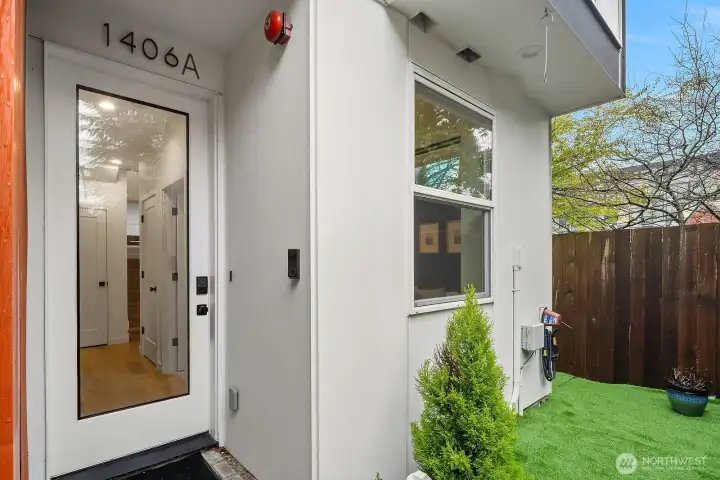 Welcoming private entry with a modern door, clean architectural lines, and a charming small turf yard offering a rare touch of outdoor greenery in this vibrant urban setting.