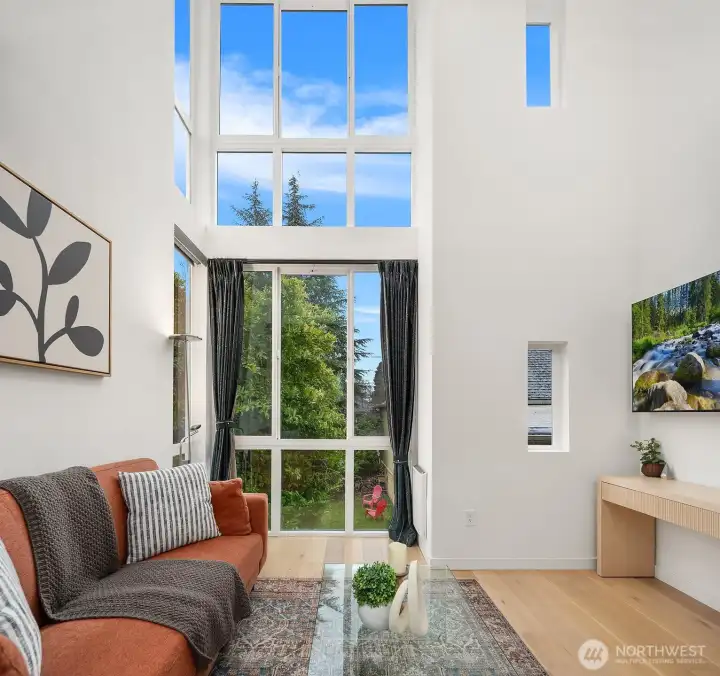 Stunning vaulted living space flooded with natural light through soaring floor-to-ceiling windows, offering a bright, open atmosphere with treetop views and effortless indoor-outdoor flow.