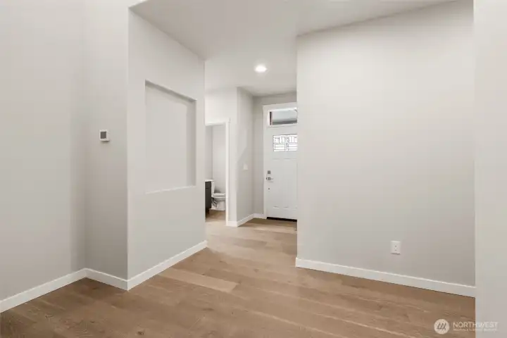 Entry way looking back to designer front door with decorative transom glass inlay showcases hallway niche and hardwood floors.