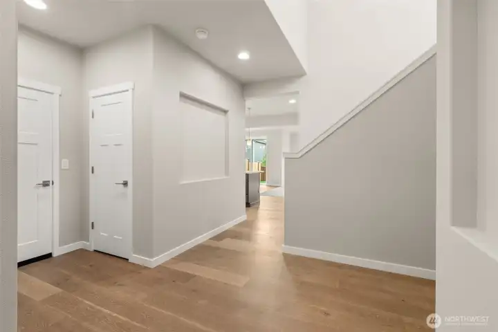 Vaulted ceiling at entryway showcases hallway niche and hardwood floors extending into kitchen and dining nook.
