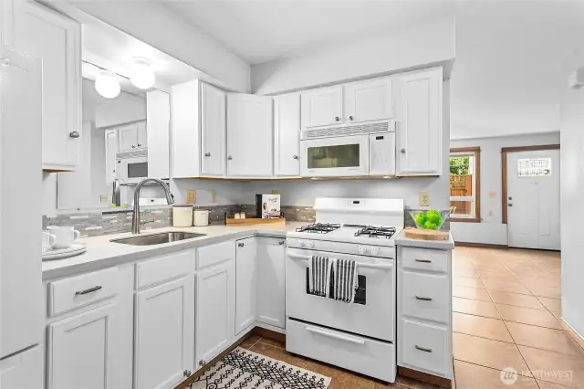 A fully equipped, self-contained kitchen with crisp, freshly painted cabinets and ceramic tile underfoot — clean, bright, and move-in ready.