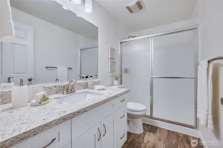 Shown here is private bath of the primary suite. The vanity is generous, with a quartz countertop and ample cupboard space.