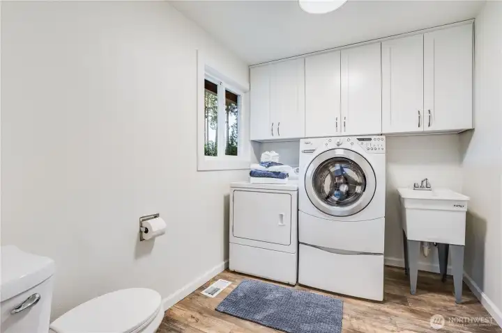 Back to the main level, the laundry room leads to the garage. Above the washer and dryer are new white cupboards. Also featured is a new toilet and utility sink.