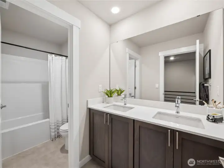 Hall bath with double sink vanity.  Notice the door separating the sink and the shower to allow multiple people to get ready for the day. Photo is representational. Actual home is under construction and finishes and colors will vary. See site agent for details.