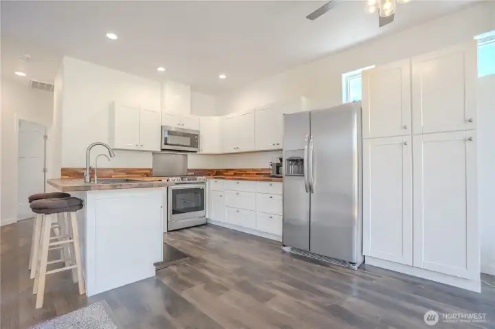 Quality white shaker cabinets, including large pantry cabinets enhance this open kitchen design. Handsome organic butcher block countertops feel. natural. Kitchen upgraded in 2024.