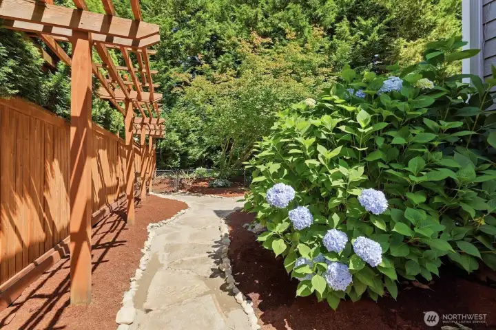 A picturesque trellis-lined walkway showcases beautiful plantings and mature greenery, adding a touch of charm and creating a peaceful garden retreat along the side of the home. A picturesque trellis-lined walkway showcases beautiful plantings and mature greenery, adding a touch of charm and creating a peaceful garden retreat along the side of the home.