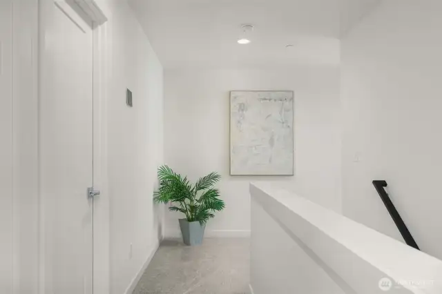The upper landing offers a bright and airy feel, complemented by a sleek modern railing and soft carpeting—a perfect space to display art or add a reading nook.