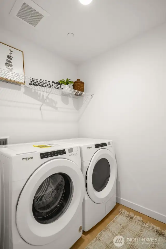 A dedicated laundry room features a Whirlpool washer and dryer, ample shelving for storage, and bright lighting for convenience.