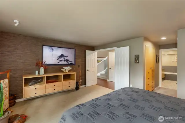 Double doors lead into the spacious primary suite featuring floating custom bedside tables and bureau. The wall-mounted TV stays with the home.