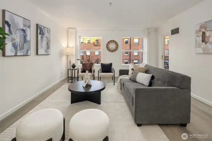 A charming living area with flexible seating options. Two large windows bring natural light into the room.