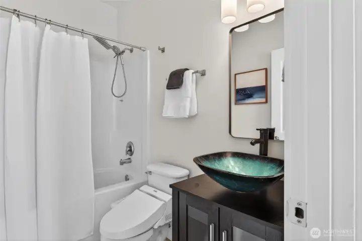 Beautifully updated bathroom with eye-catching turquoise glass vessel sink, dark vanity, and clean modern finishes.
