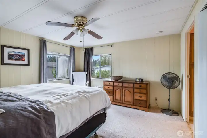 Large windows fill the bedroom with natural light, complemented by soft carpet underfoot.
