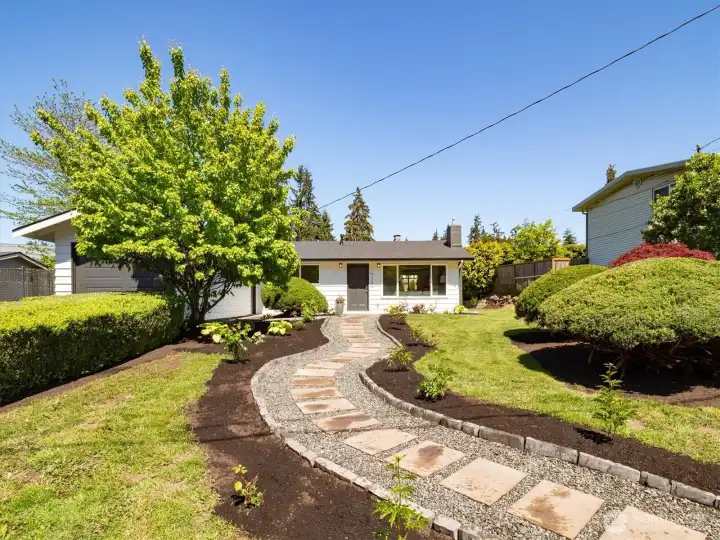 Curved walkway and mature greenery create a private, inviting approach to this well-maintained rambler. Image is from earlier listing in Sep 2025.