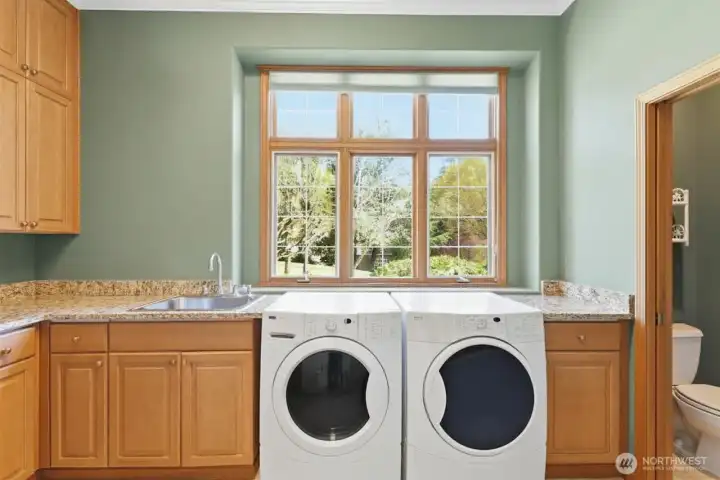 A large laundry room with slab granite counters, abundant cabinetry, laundry ink and 1/2 bath.